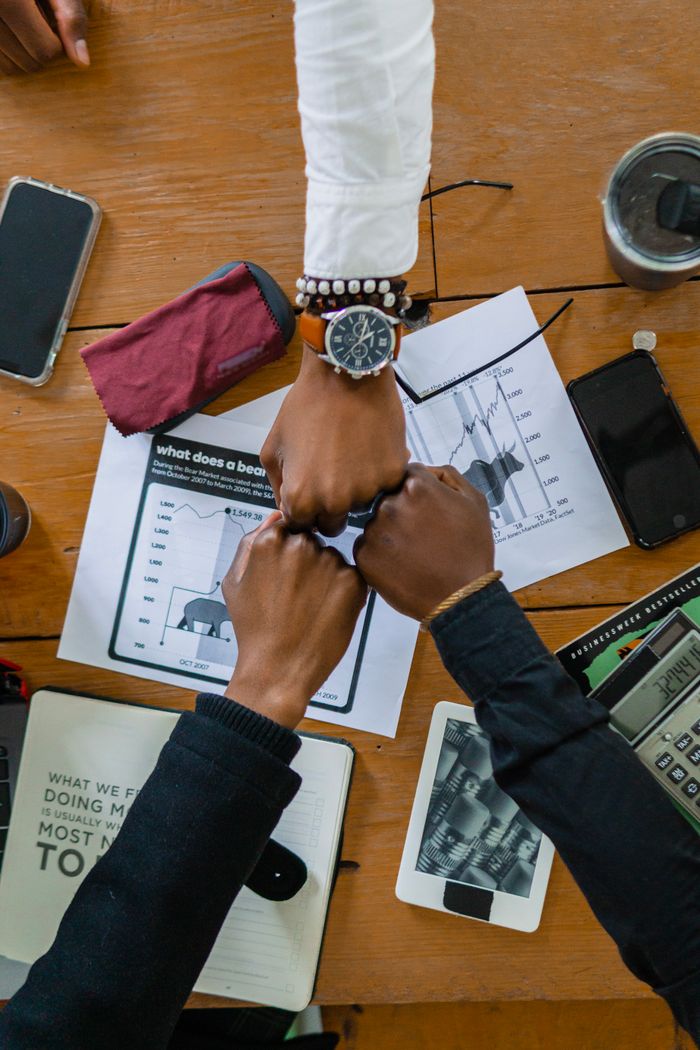 Crafting Captivating Headlines: Your awesome post title goes here Coworkers joining fists over office desk, symbolizing teamwork and motivation.